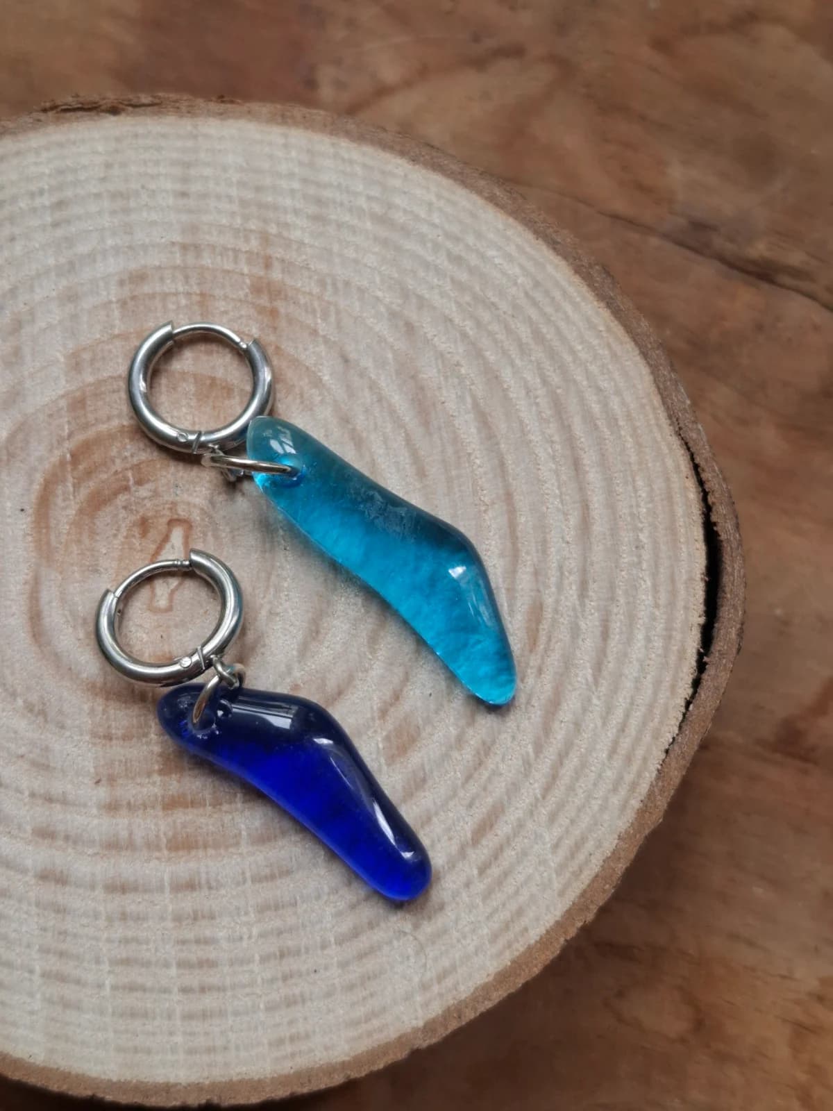 Boucles d'oreilles en verre bleu turquoise et cobalt posées sur un rondin de bois.