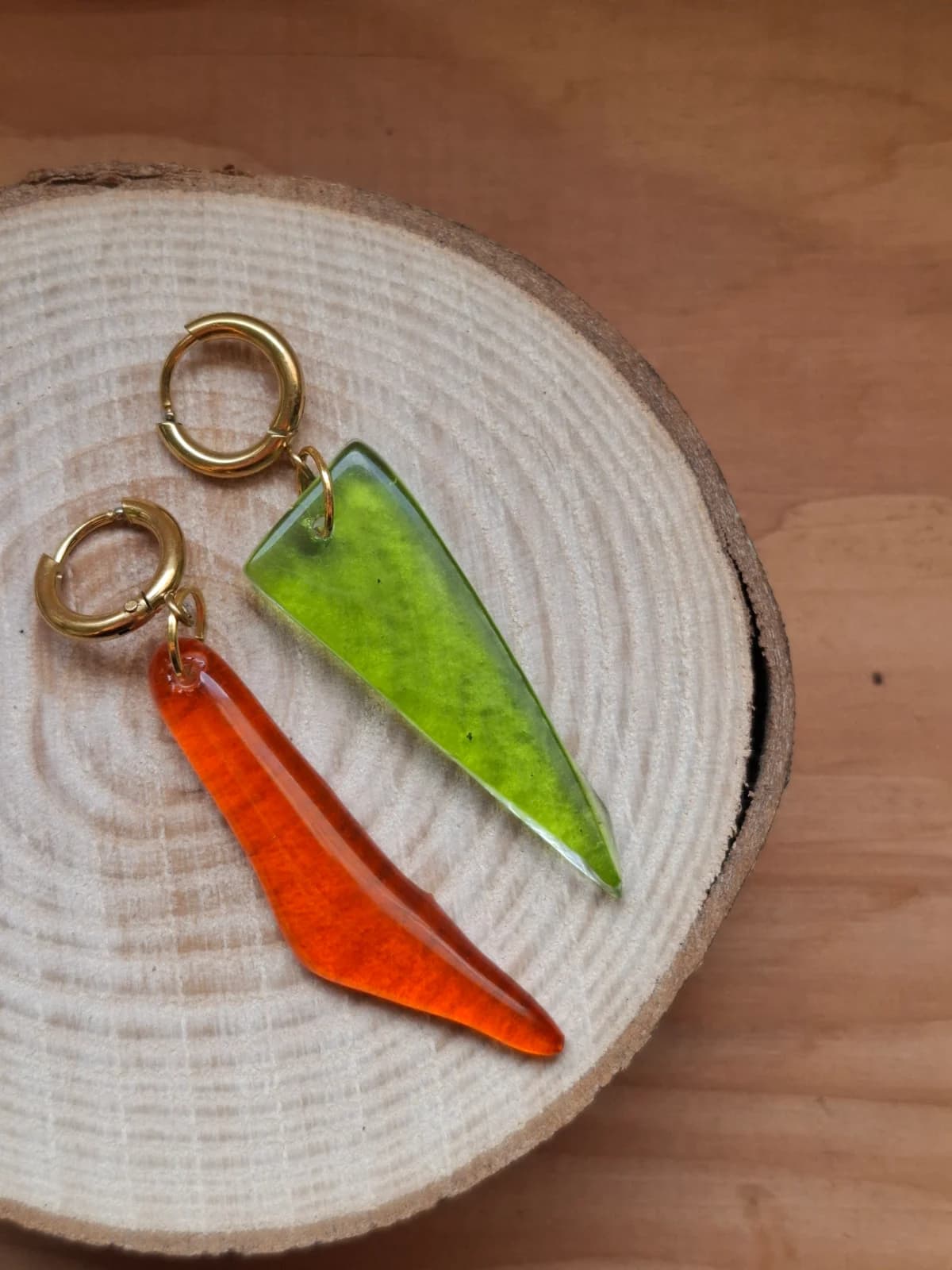 Boucles d’oreilles asymétriques en verre vert et orange posées sur une rondelle de bois