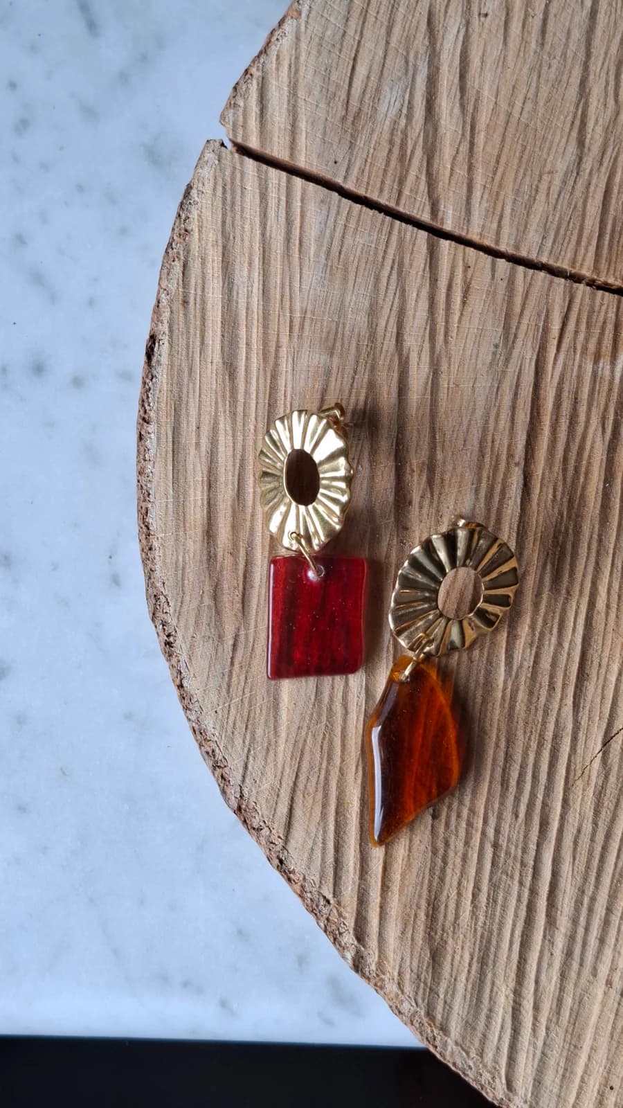 Boucles d'oreilles dorées avec pendentifs en verre rose et orange posées sur une tranche de bois.