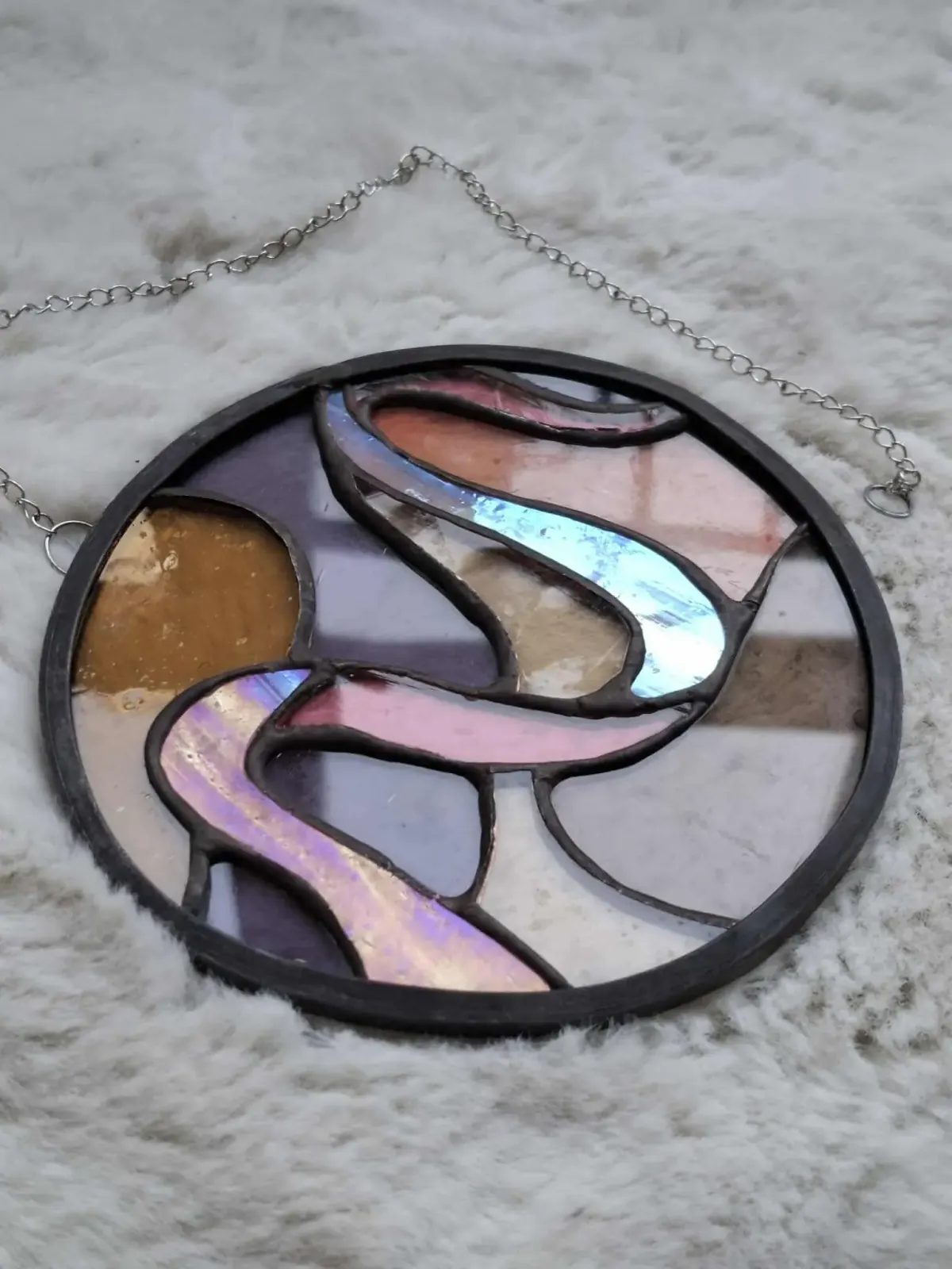 Vitrail rond suspendu aux formes ondulées dans les tons rose, violet et ambré avec soudures noires.
