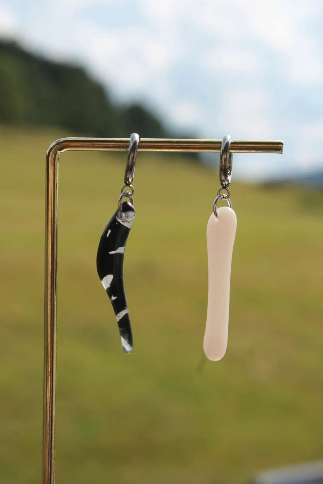 Boucles d'oreilles pendantes asymétriques, une noire et une blanche, suspendues à un présentoir métallique.