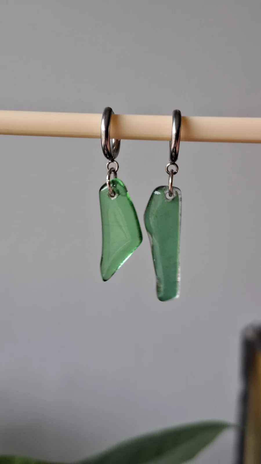 Paire de boucles d'oreilles dormeuses avec éclats de verre vert transparent suspendues à un support.