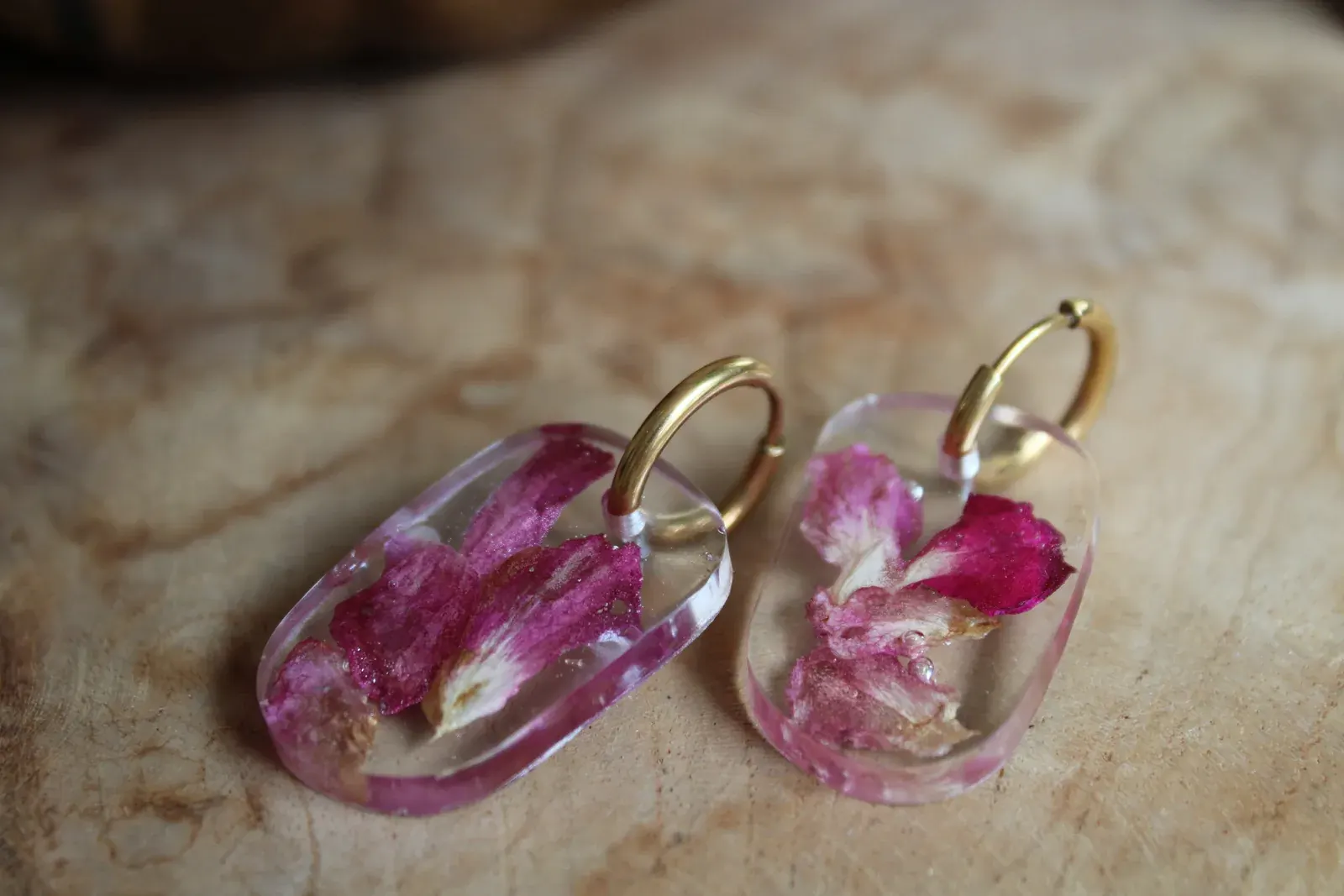 Boucles d'oreilles dorées avec pendentifs transparents et pétales de fleurs roses séchés posées à plat