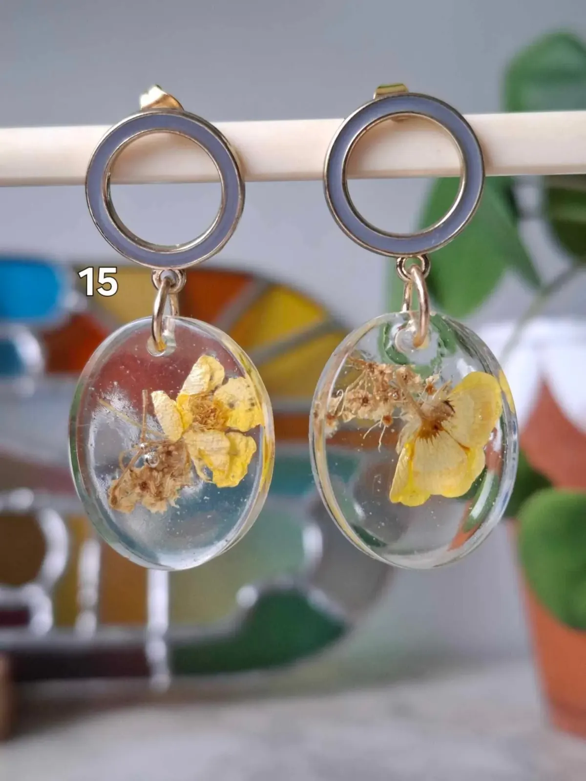 Boucles d'oreilles pendantes ovales en résine transparente avec fleurs jaunes séchées et anneaux dorés gris.