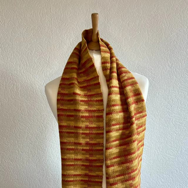 Écharpe tissée à motifs jaune doré et orangé drapée sur un buste de mannequin.