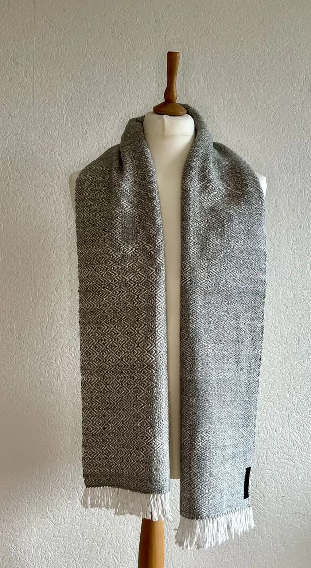 Écharpe tissée grise et blanche à motifs géométriques et franges, présentée sur un mannequin