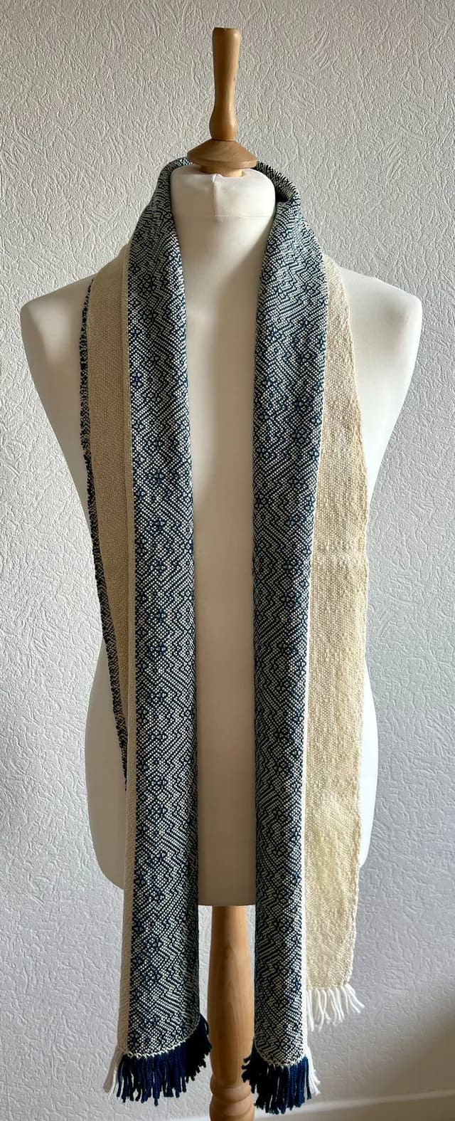 Écharpe bicolore écru et bleu à motifs géométriques et franges, présentée sur un buste de couture.