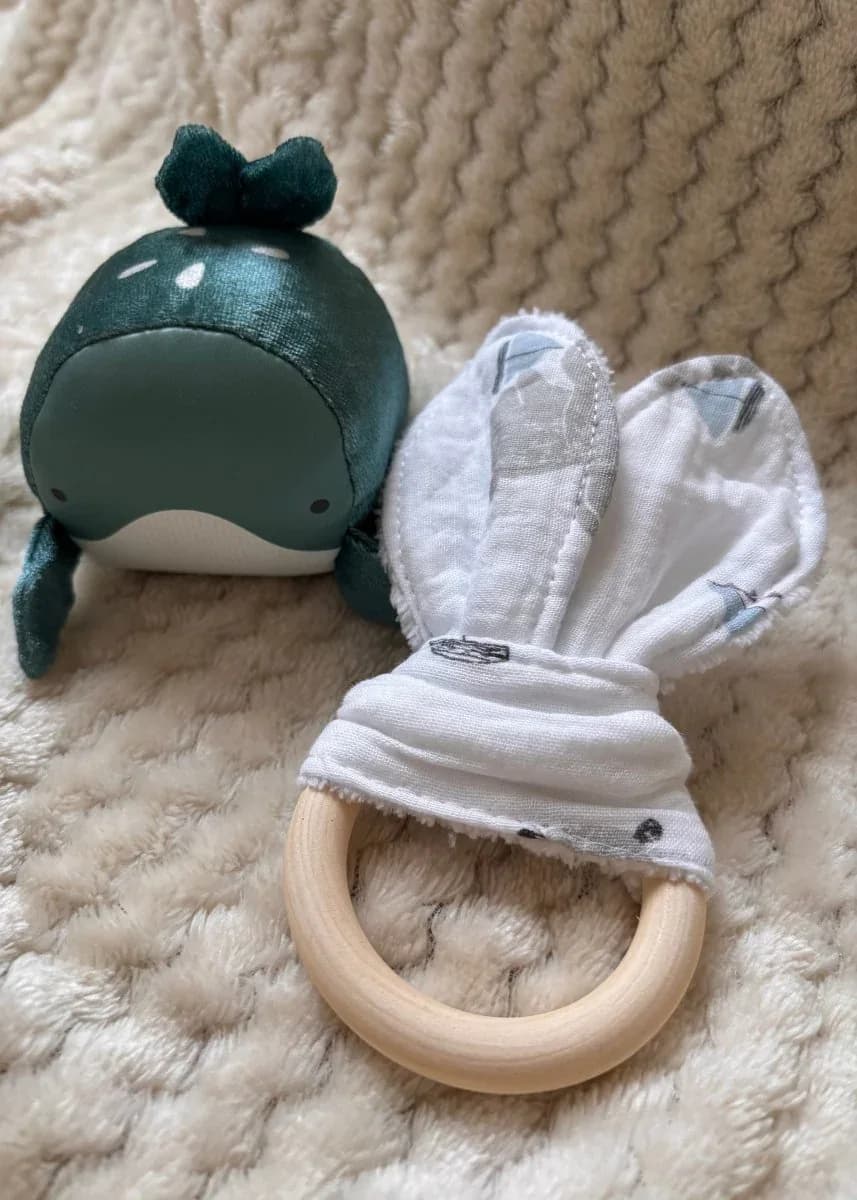 Anneau de dentition en bois avec tissu oreilles de lapin blanc et peluche baleine verte sur plaid doux