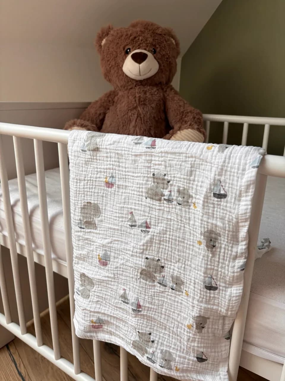 Lange blanc à motifs d'animaux et bateaux posé sur un lit à barreaux d'enfant avec un ours en peluche