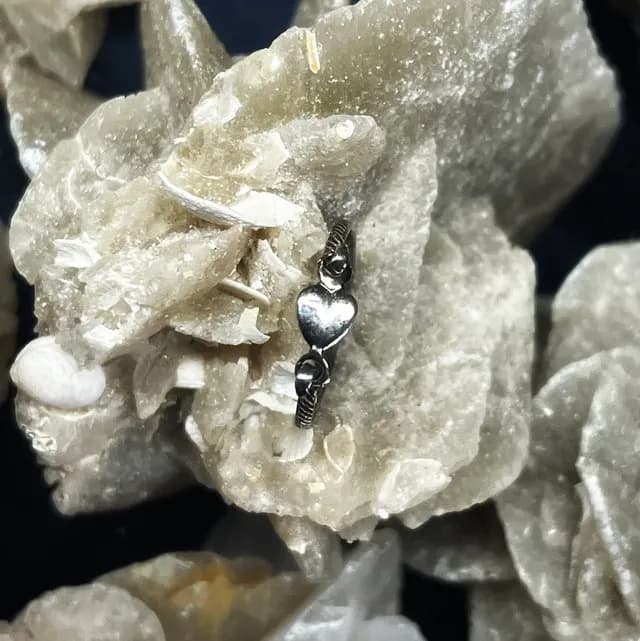 Bague fine en argent ornée d'un motif cœur posée sur une roche minérale