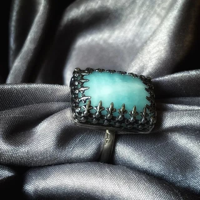 Bague en argent avec pierre rectangulaire bleu clair posée sur tissu satiné