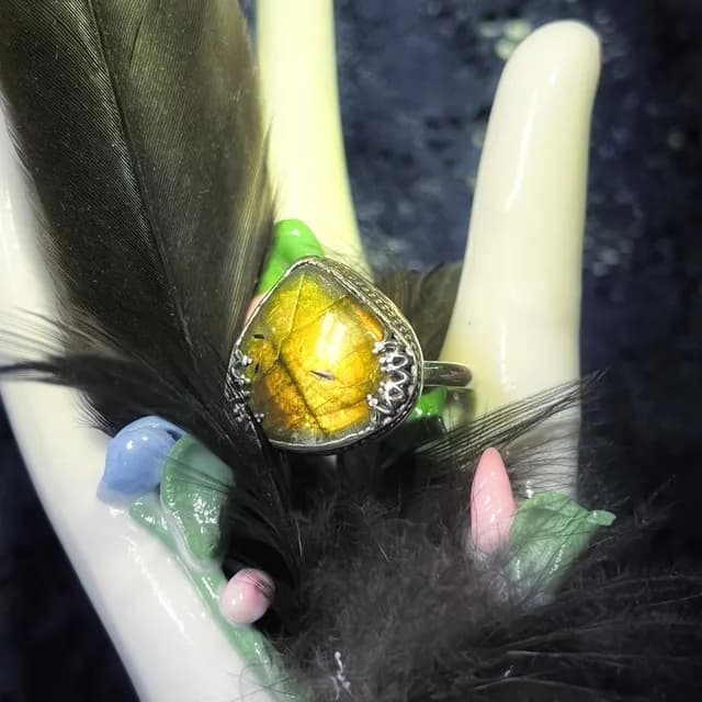 Bague en argent avec labradorite triangulaire aux reflets dorés, posée sur une main décorative