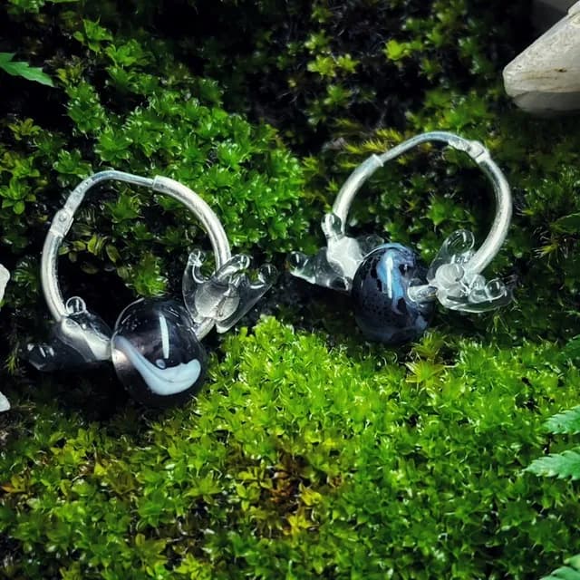 Créoles en argent et perles en verre noir et bleu aux détails transparents posées sur de la mousse
