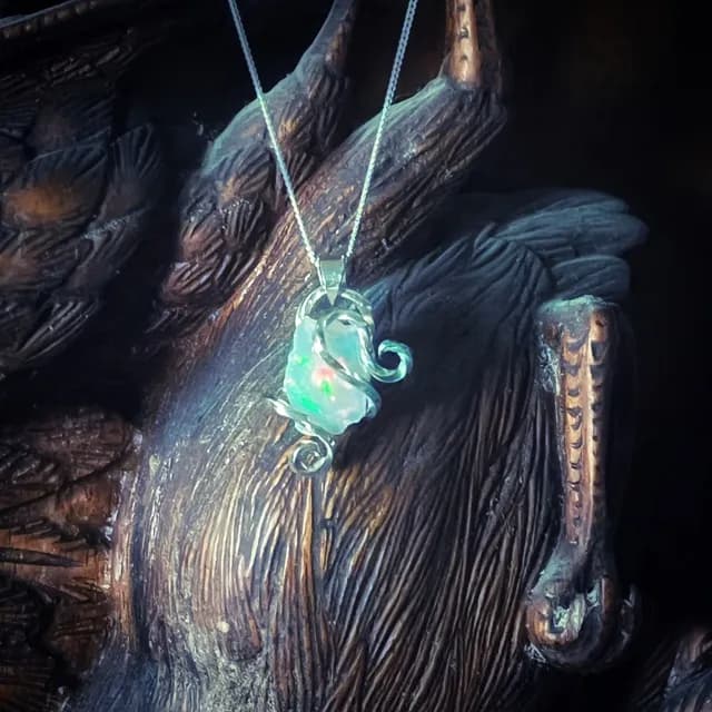Pendentif en opale irisée serti de volutes en argent 925 sur fond de bois sculpté.