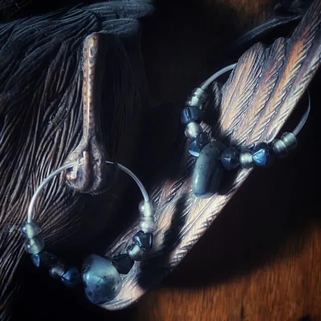 Créoles en argent ornées de perles sombres et d'une agate naturelle, posées sur une sculpture en bois.
