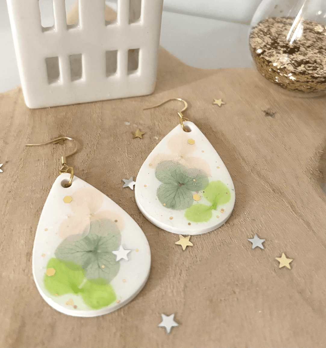 Gros plan sur les boucles d'oreilles en goutte blanches aux fleurs d'hortensia vertes et dorures.