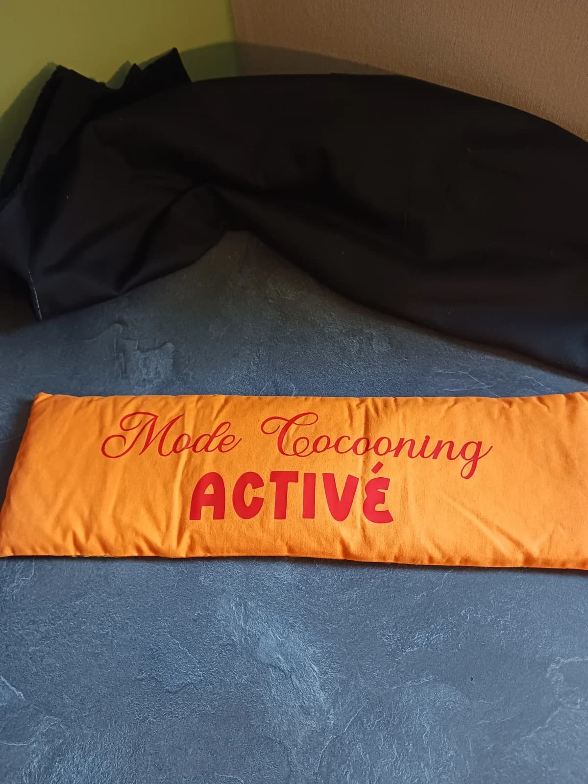 Bouillotte de blé longue en tissu orange avec le texte rouge Mode Cocooning ACTIVÉ posée à plat.