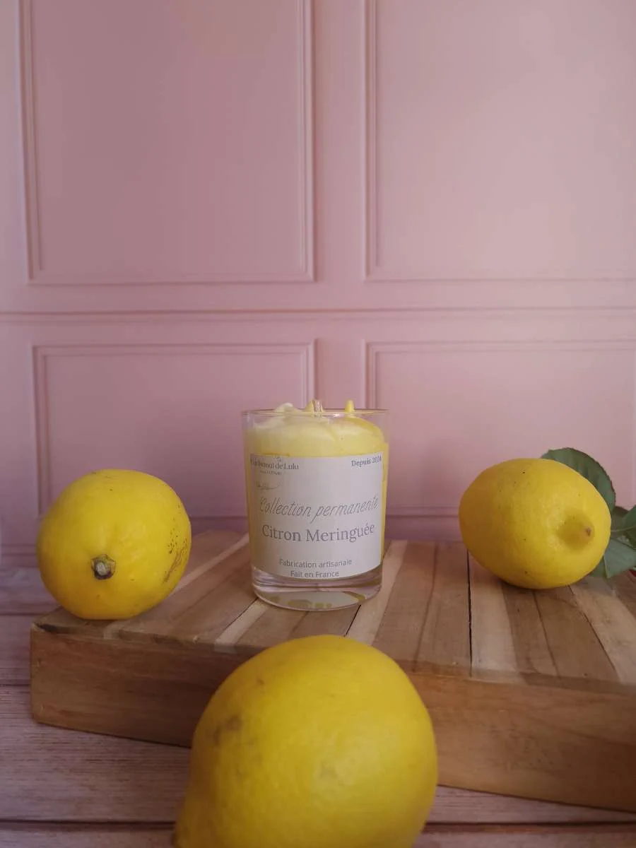 Bougie parfumée en verre transparent aux nuances jaune et blanche, entourée de citrons sur socle en bois.