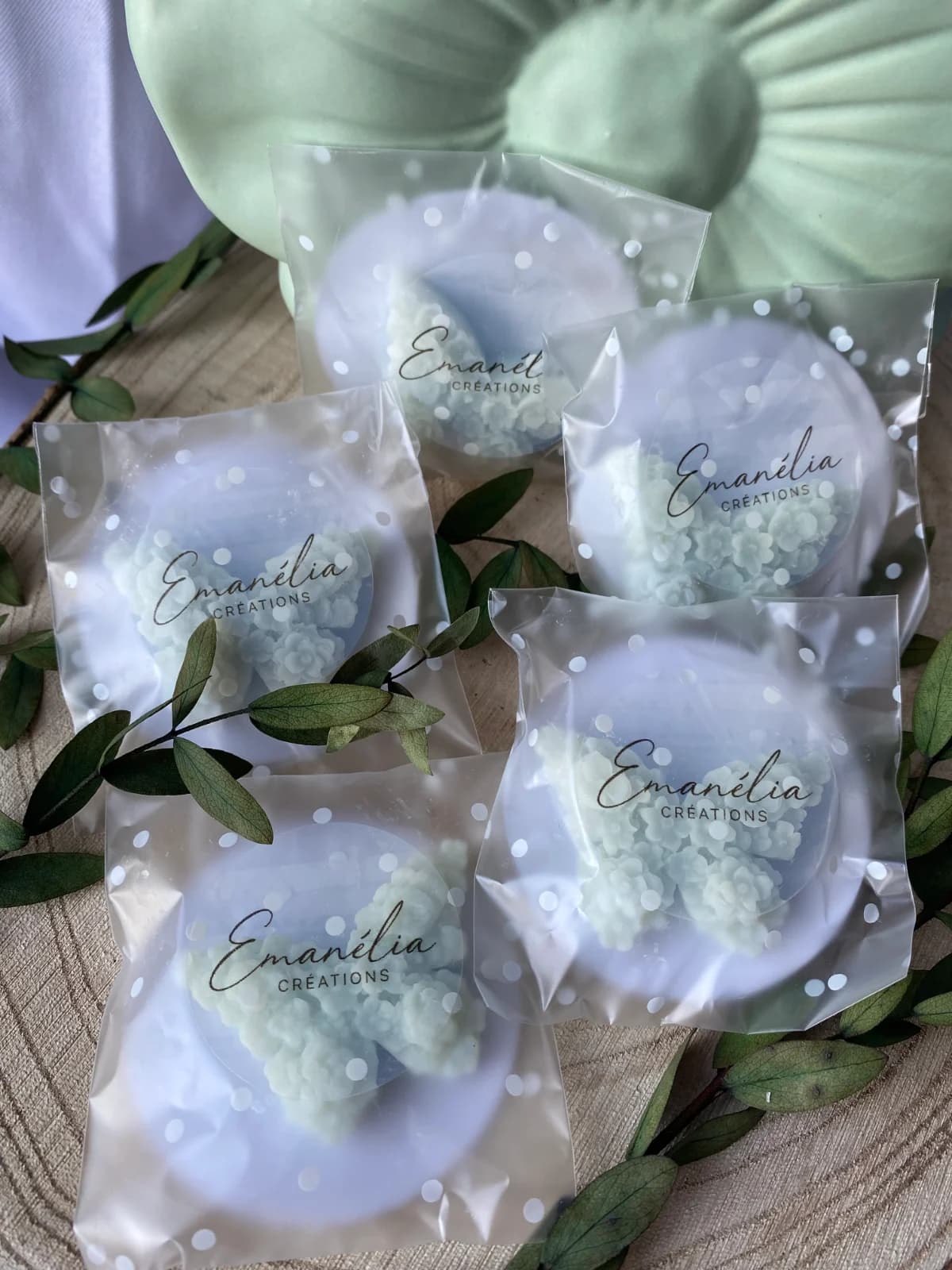 Fondants de cire blanche en forme de papillon fleuri emballés individuellement avec du feuillage vert.