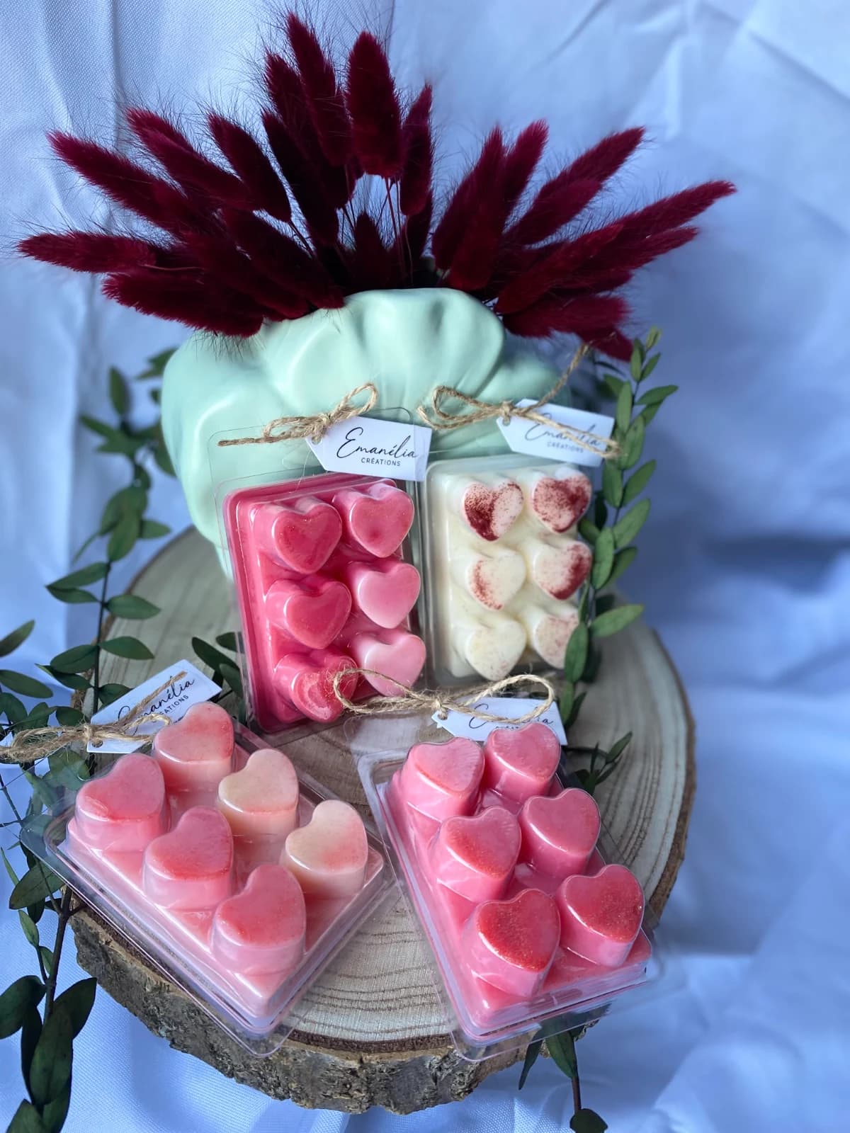 Quatre clamshells de cire parfumée en forme de cœurs roses et blancs sur un socle en bois.