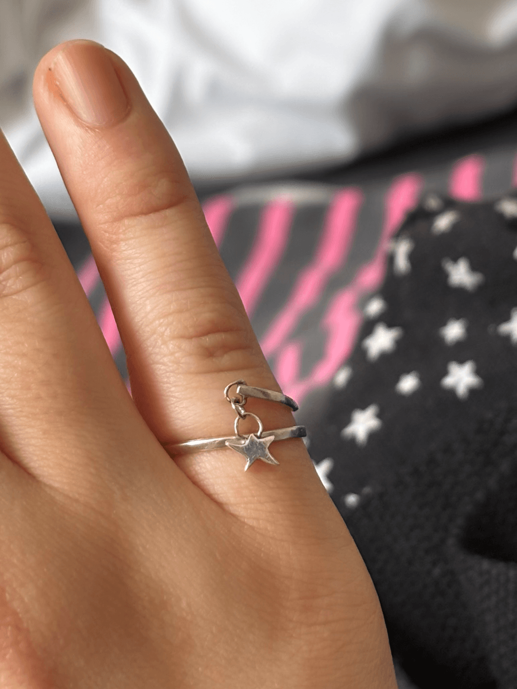Bague fine argentée portée au doigt, ornée d’une petite breloque en forme d’étoile suspendue.